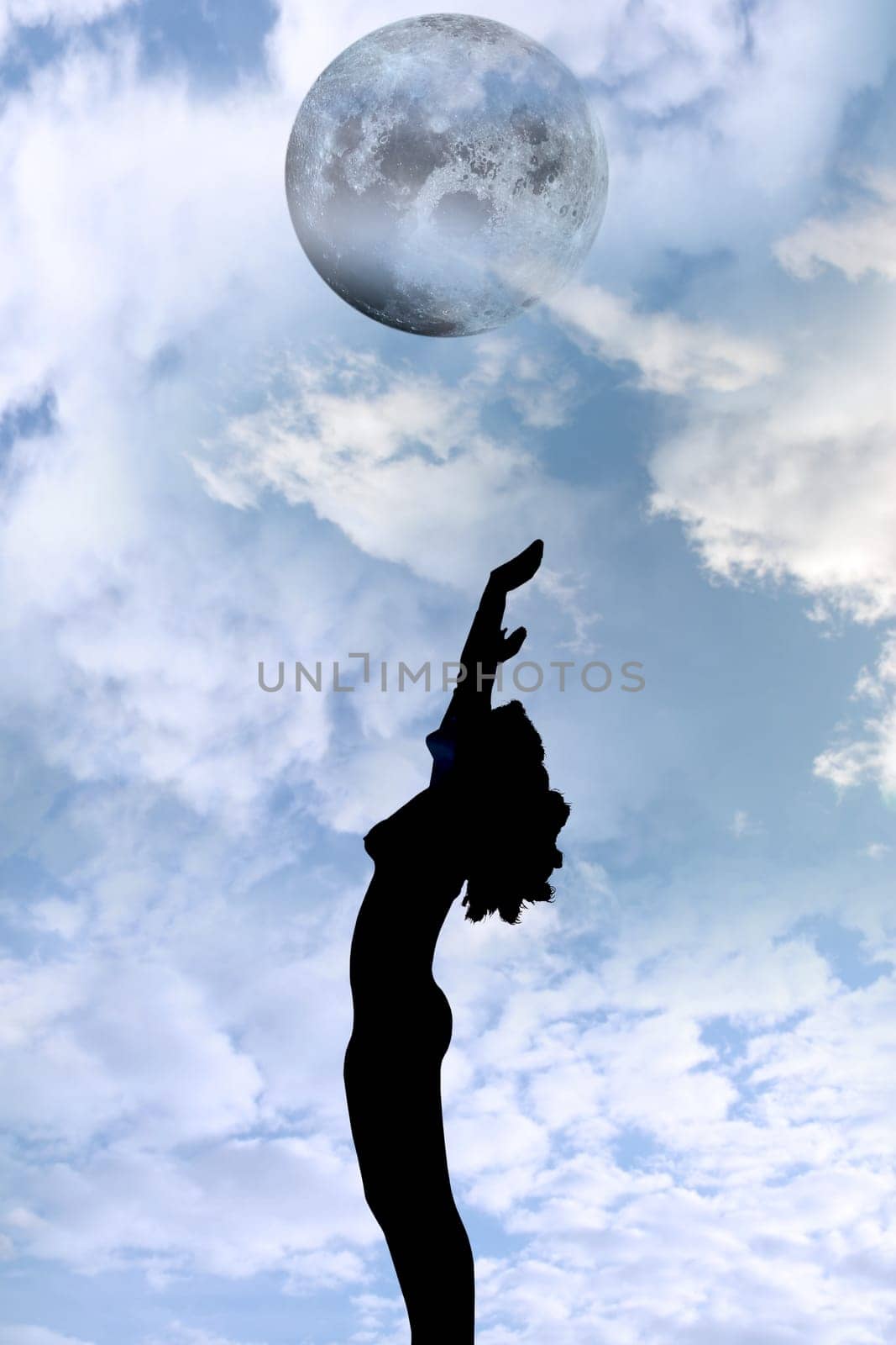 attractive silhouetted nude woman holding her hands up to the sky giving gratitude to the moon in a yoga pose with a cloudy background