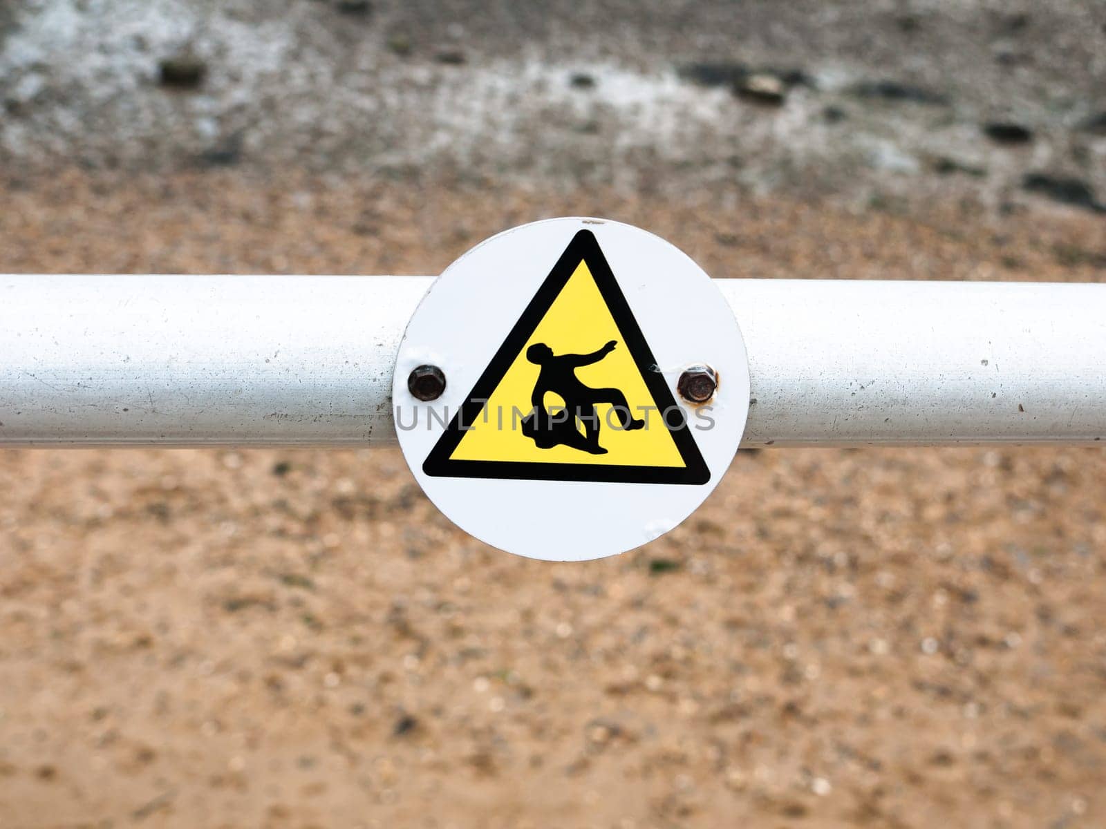 a funny sign on pole indicated a man slipping, slippery surface sea front  England  UK