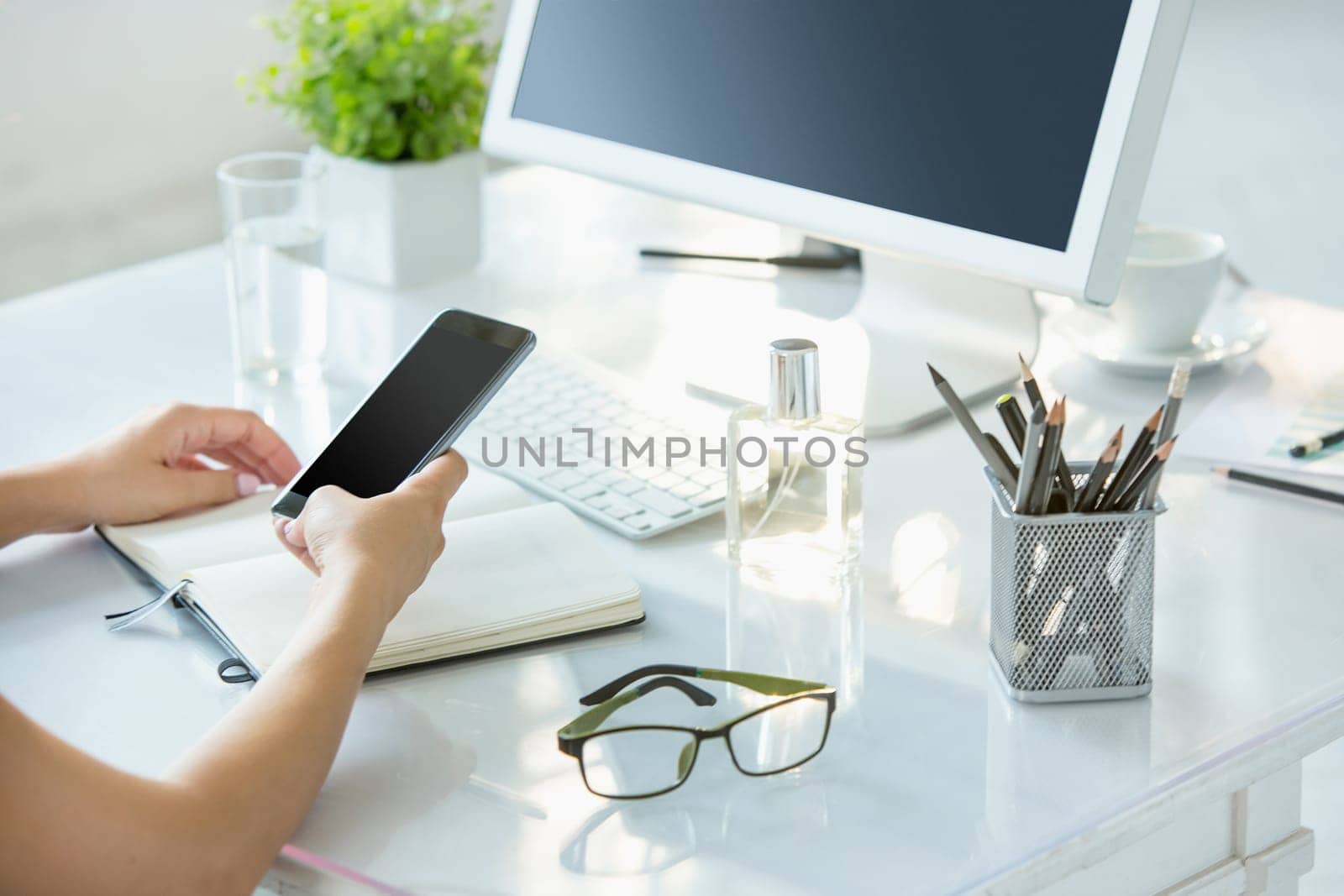 The female hands using smart phone while working on computer at modern office interior, businesswoman concept