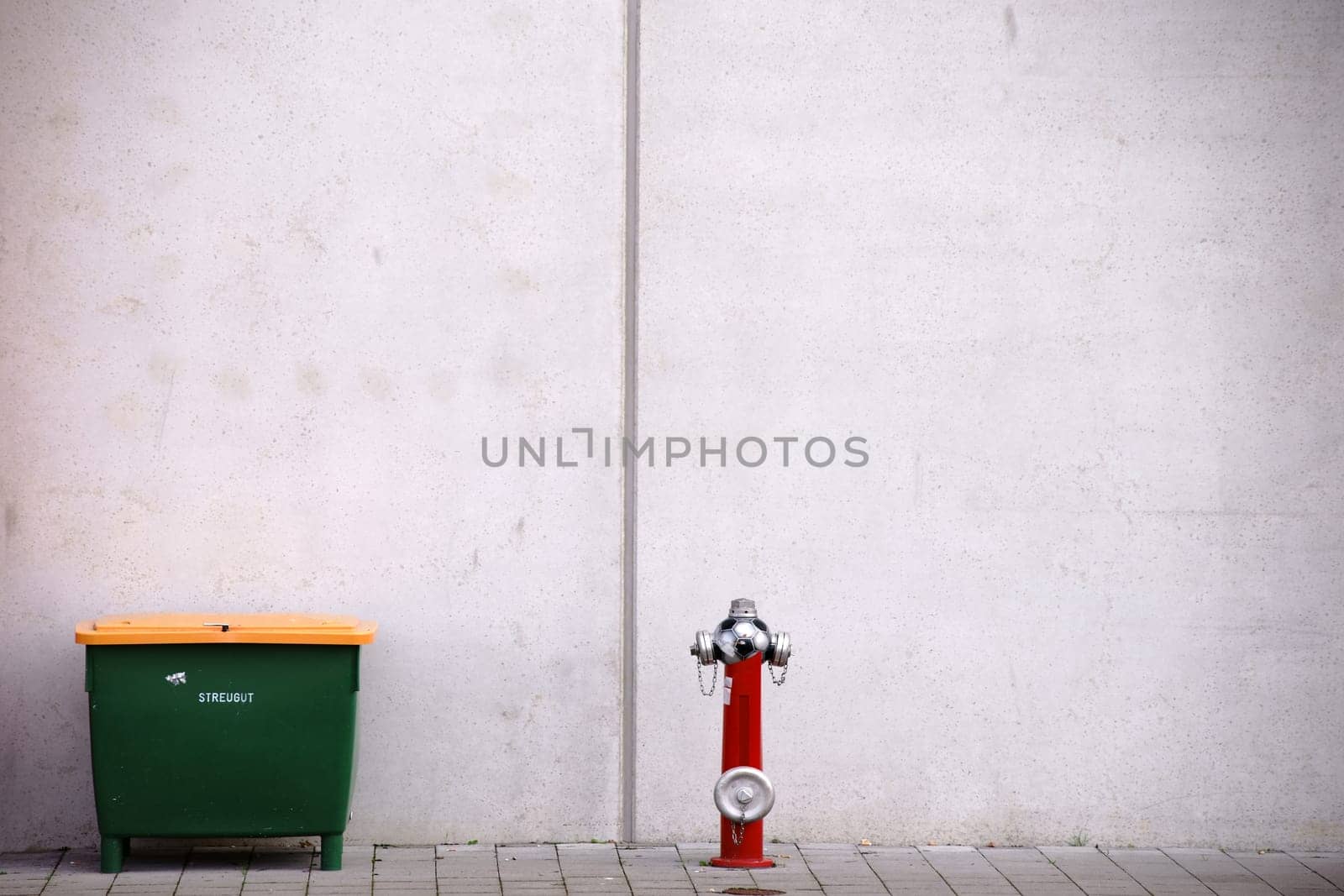 A grit container and a fire hydrant in front of the striking concrete façade of a stadium.