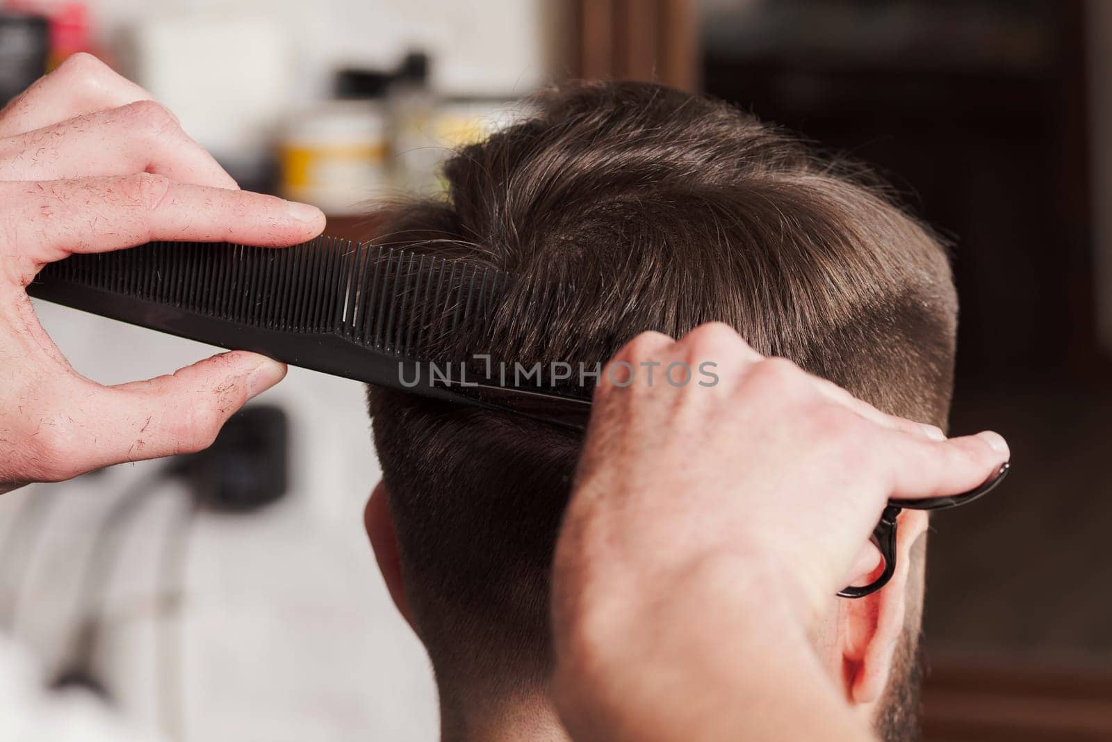 The hands of barber making haircut to attractive man in barbershop