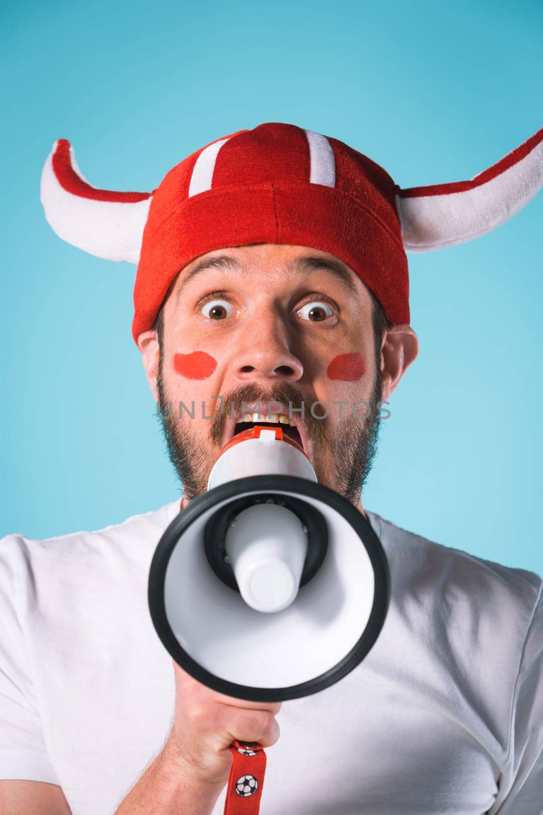 The football fan with megaphone over blue. The young man looking at camera with different emotions on face