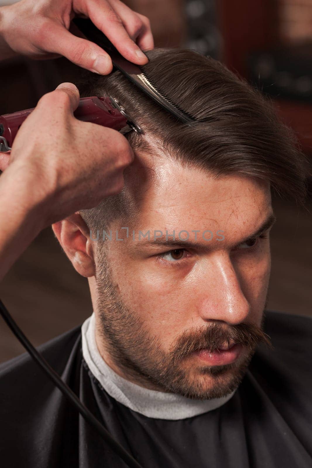 The hands of barber making haircut to attractive man in barbershop