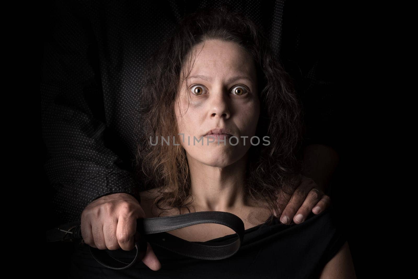 Abused woman victim of domestic violence, with husband hand holding a belt as a weapon.