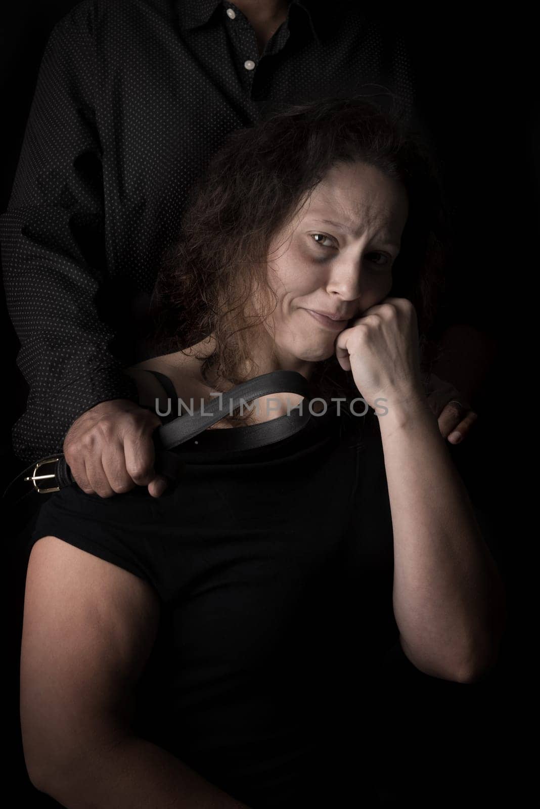 Abused woman victim of domestic violence, with husband hand holding a belt as a weapon.