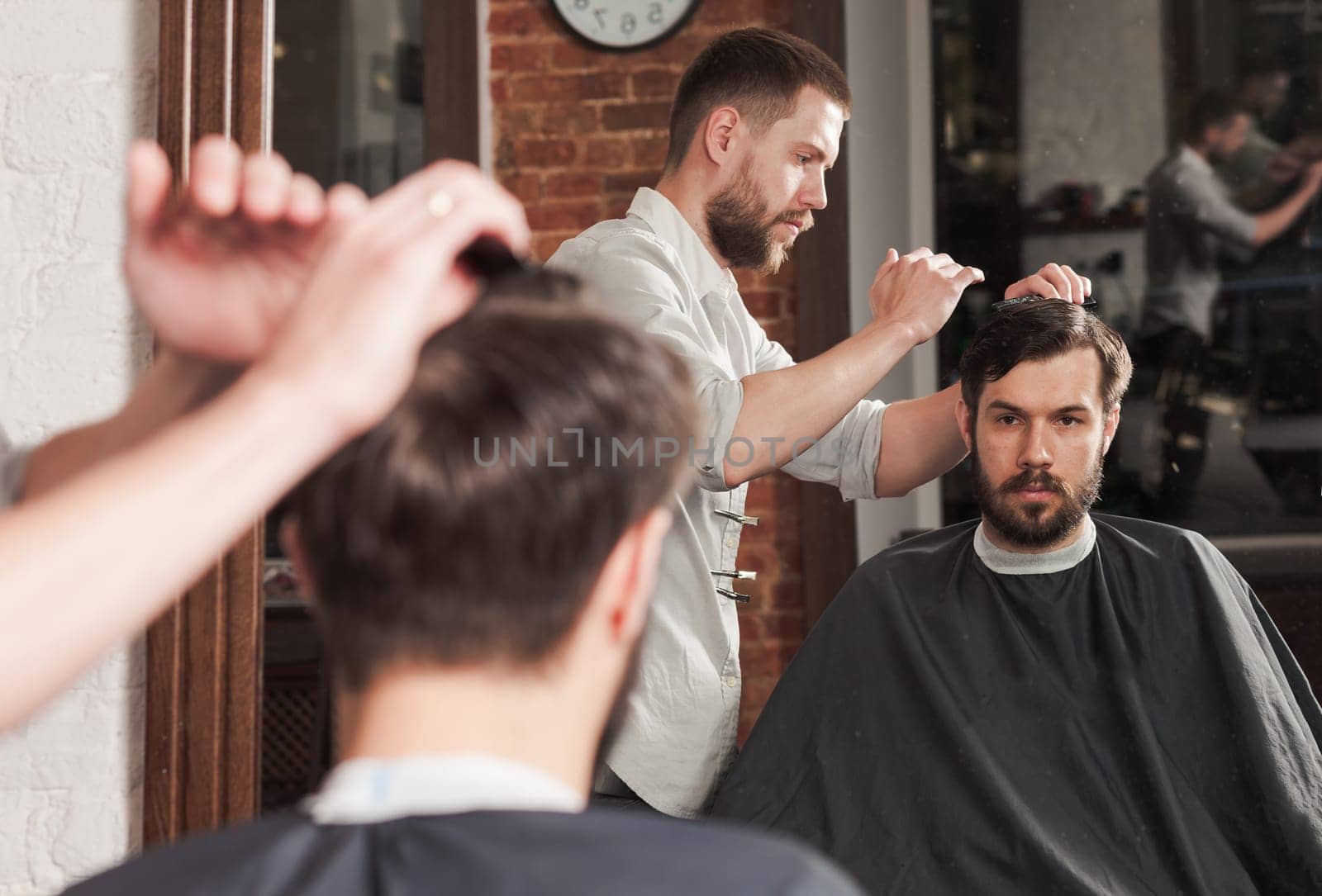 Young handsome barber making haircut of attractive bearded man in barbershop