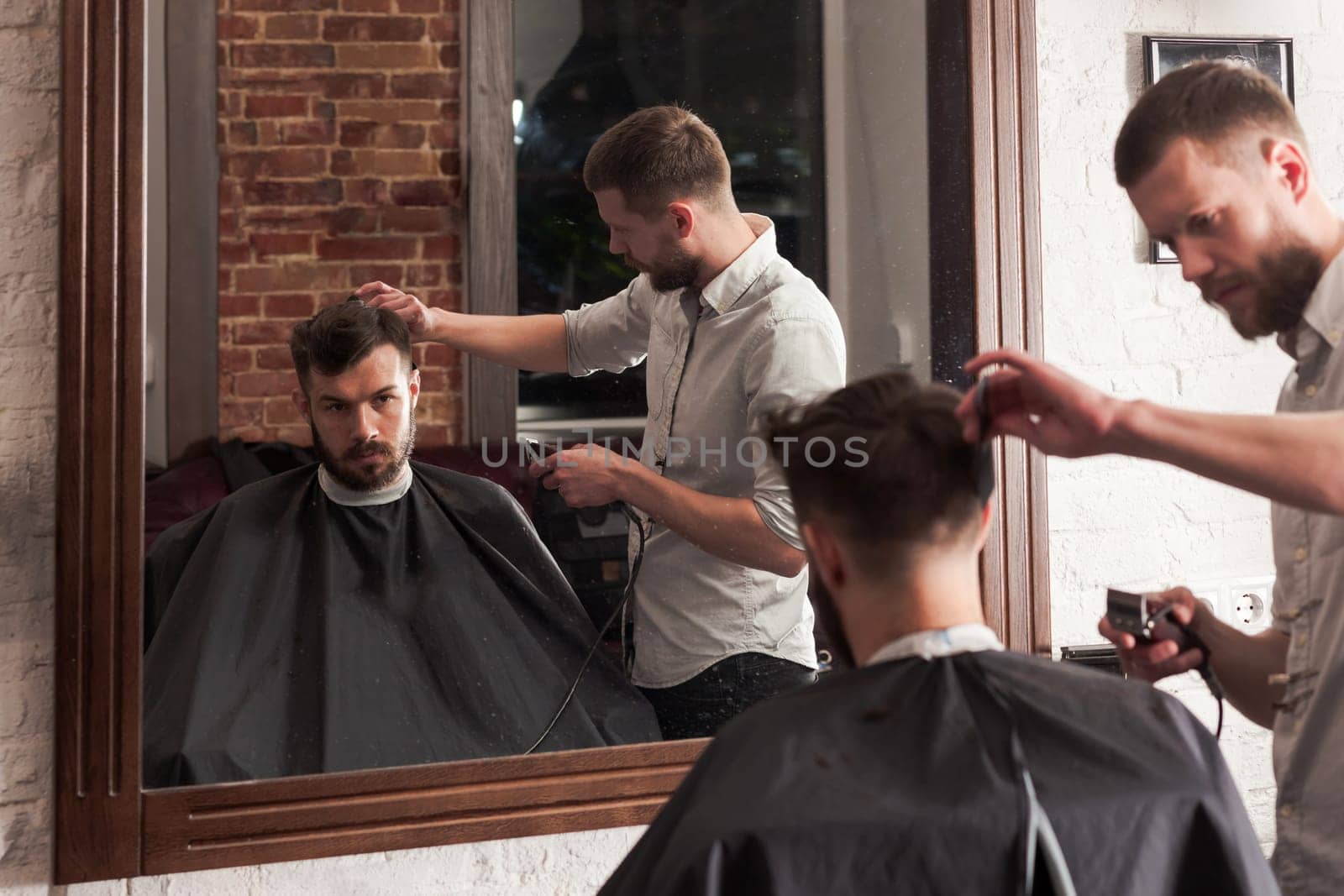 Young handsome barber making haircut of attractive bearded man in barbershop