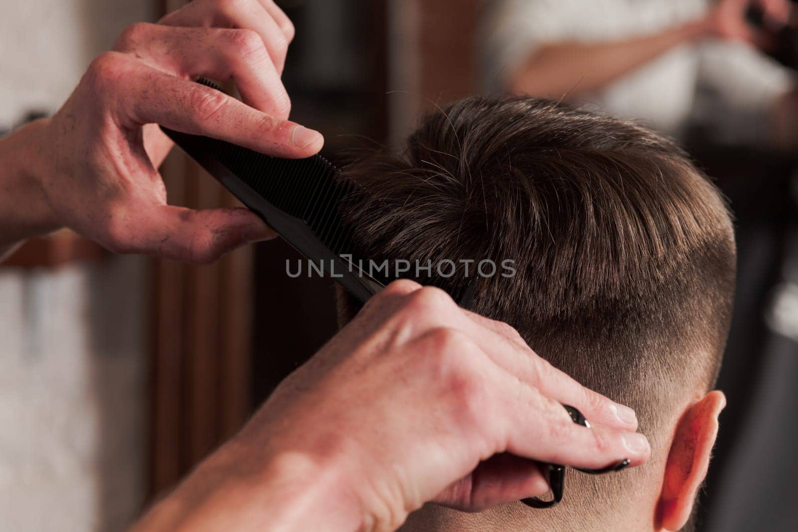 The hands of barber making haircut to attractive man in barbershop