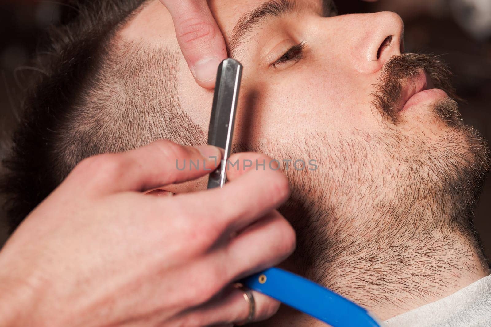 Hipster client visiting barber shop. The hands of young barber making the cut of beard