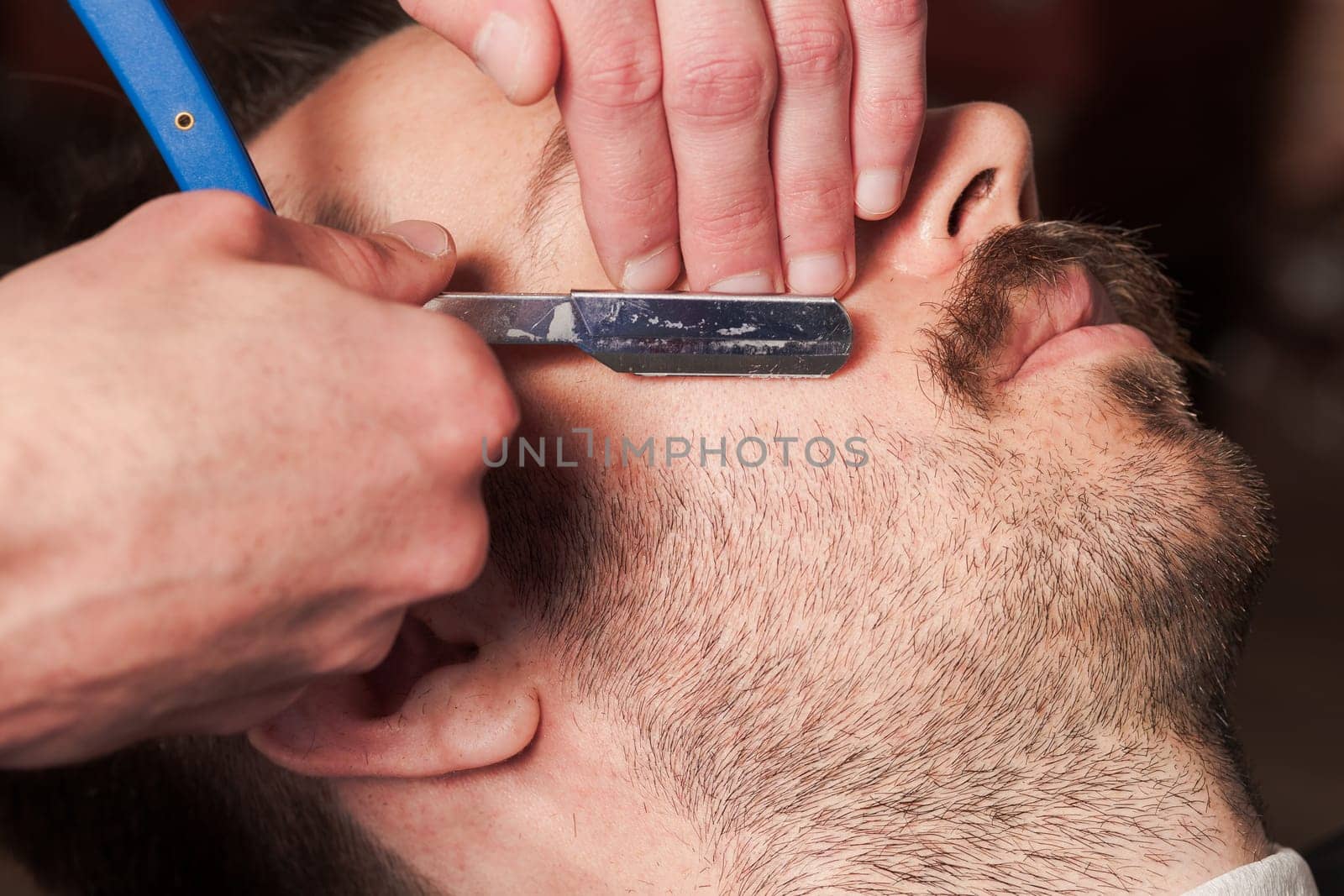 Hipster client visiting barber shop. The hands of young barber making the cut of beard