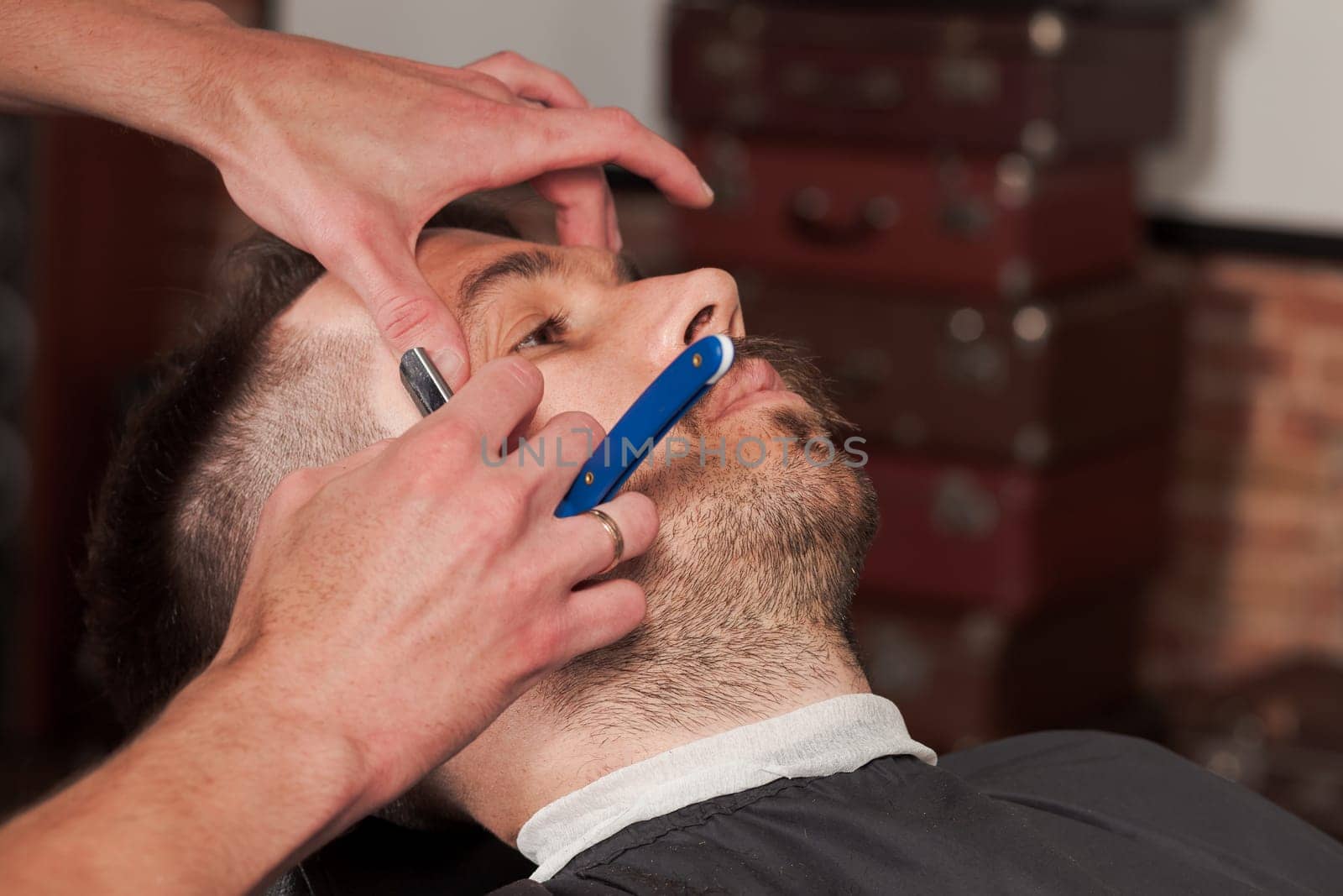 Hipster client visiting barber shop. The hands of young barber making the cut of beard