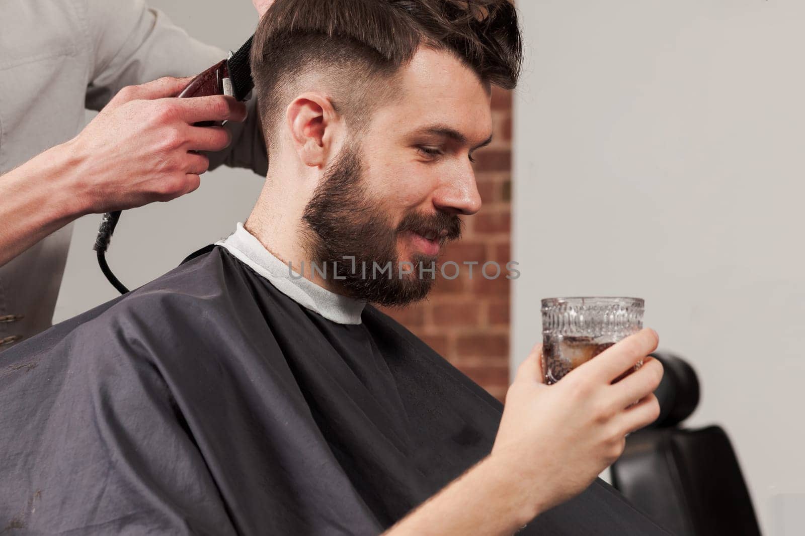 The hands of barber making haircut to attractive man in barbershop