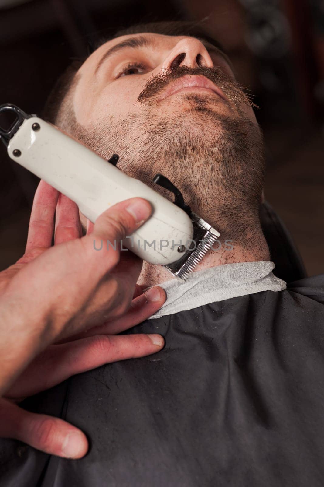 Hipster client visiting barber shop. The hands of young barber making the cut of beard