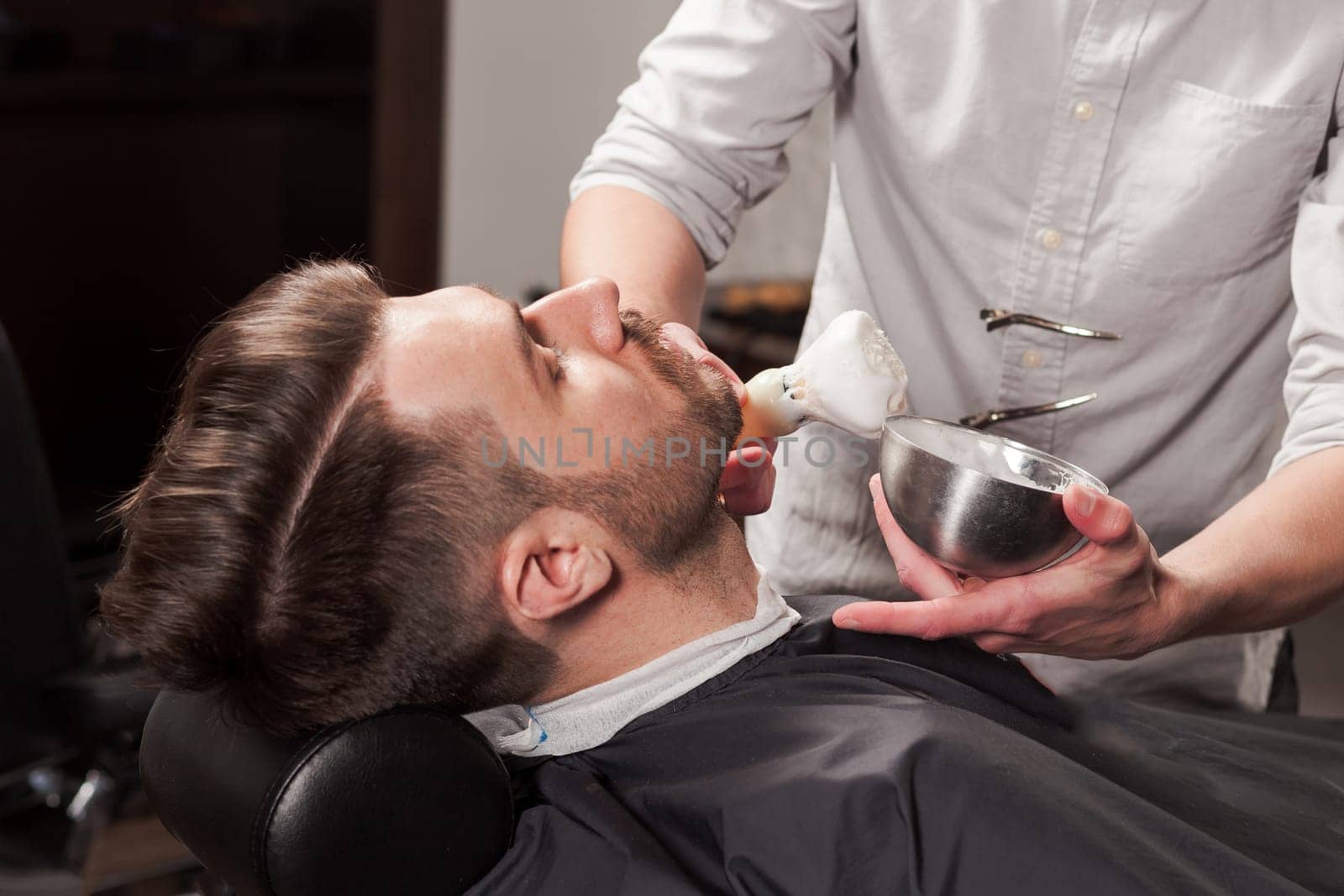 Hipster client visiting barber shop. The hands of young barber making the cut of beard