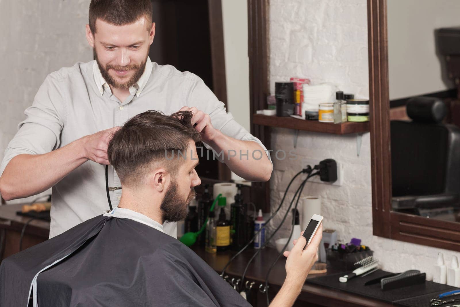 Young handsome barber making haircut of attractive bearded man in barbershop