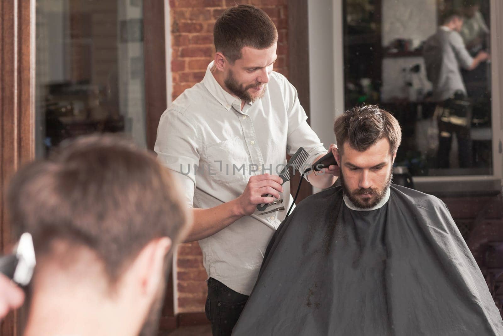 Young handsome barber making haircut of attractive bearded man in barbershop