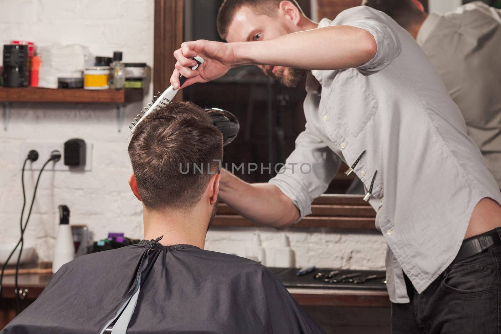 Young handsome barber making haircut of attractive bearded man in barbershop