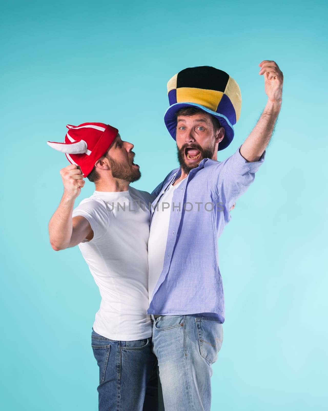 Two excited male friends celebrate watching sports on television over blue studio