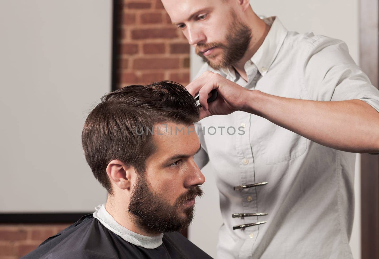 Young handsome barber making haircut of attractive bearded man in barbershop