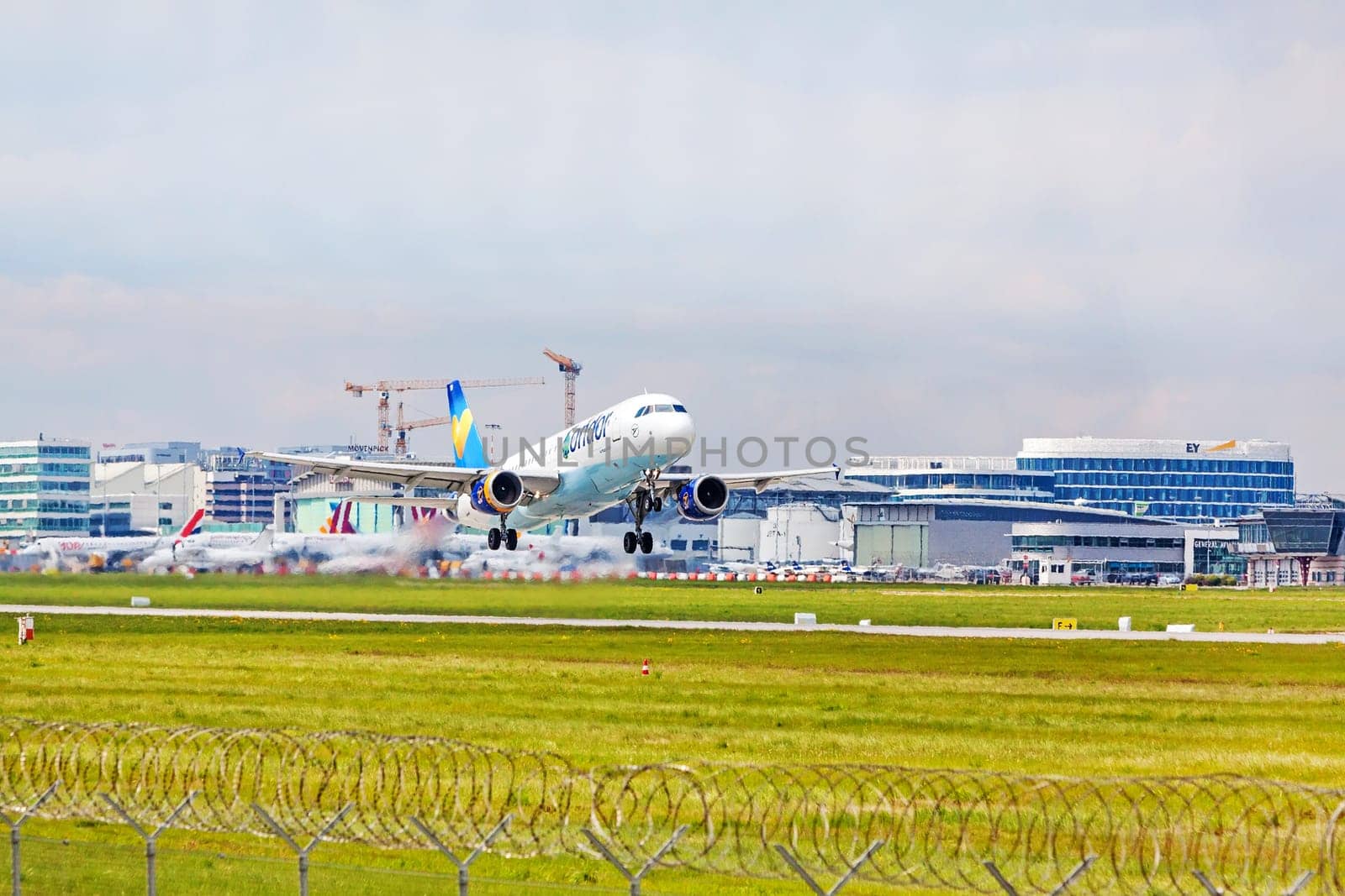 Stuttgart, Germany - April 29, 2017: Airbus airplane A320 from Condor at takeoff from runway - airport Stuttgart terminal in background - green meadow with fence in front