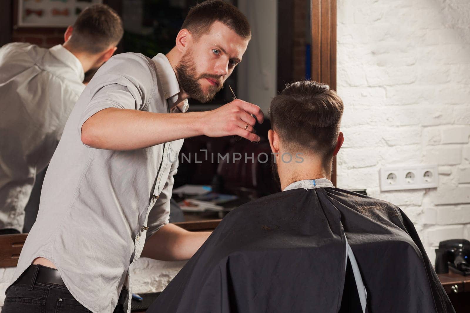 Young handsome barber making haircut of attractive bearded man in barbershop