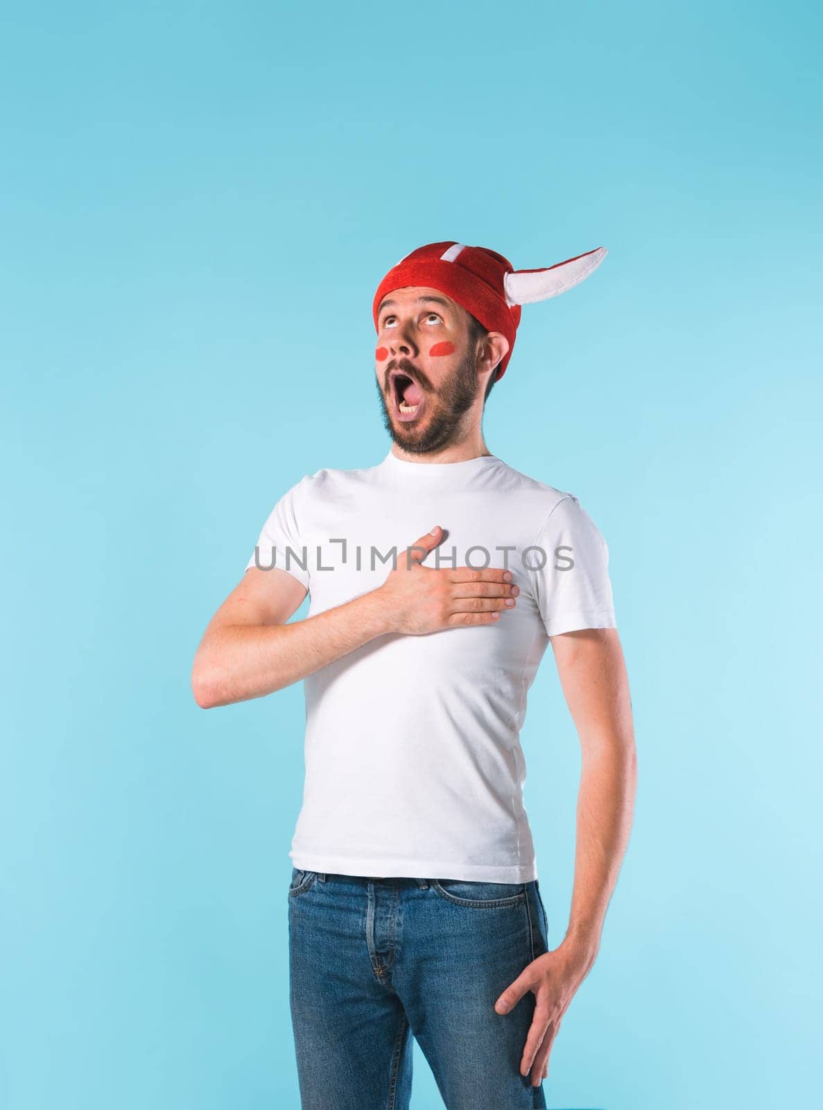 The football fan with megaphone over blue. The young man looking at camera with different emotions on face