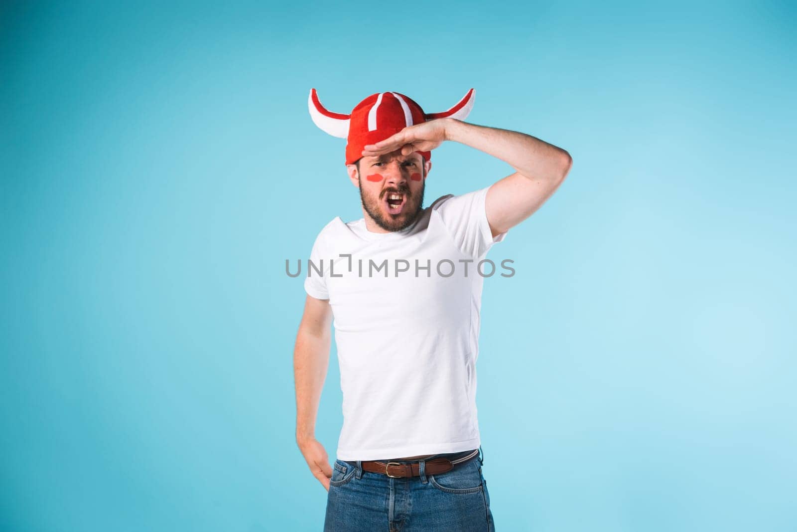 The football fan with megaphone over blue. The young man looking at camera with different emotions on face