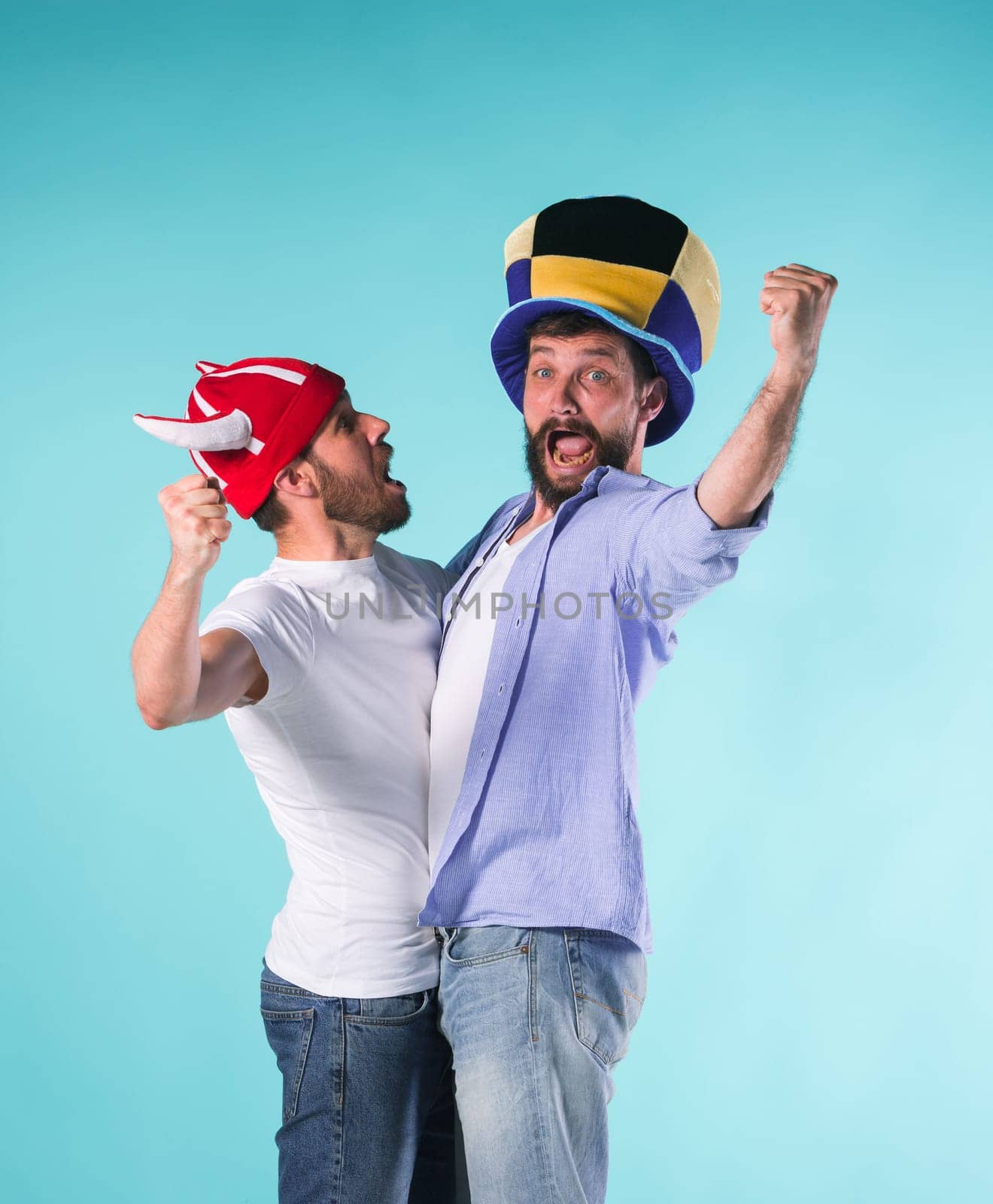 Two excited male friends celebrate watching sports on television over blue studio