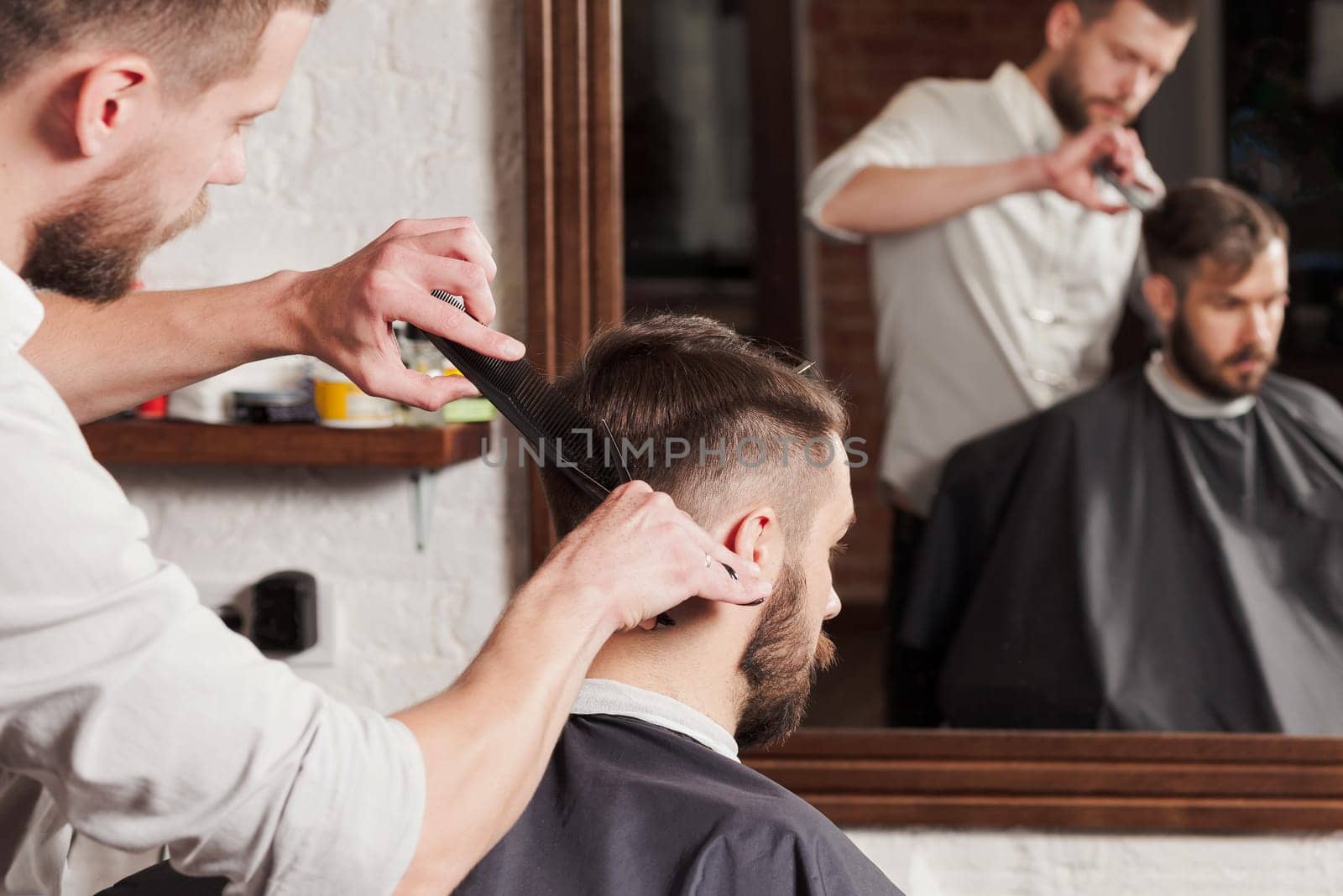 Young handsome barber making haircut of attractive bearded man in barbershop