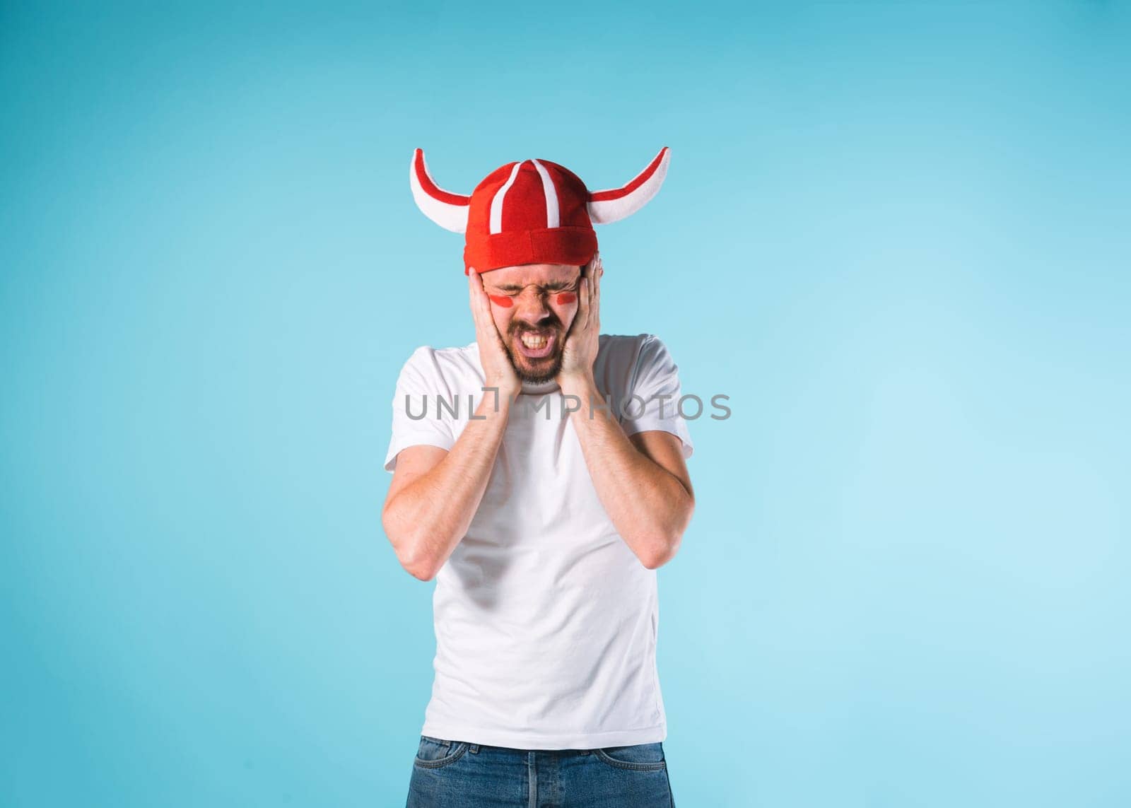 The football fan with megaphone over blue. The young man looking at camera with different emotions on face