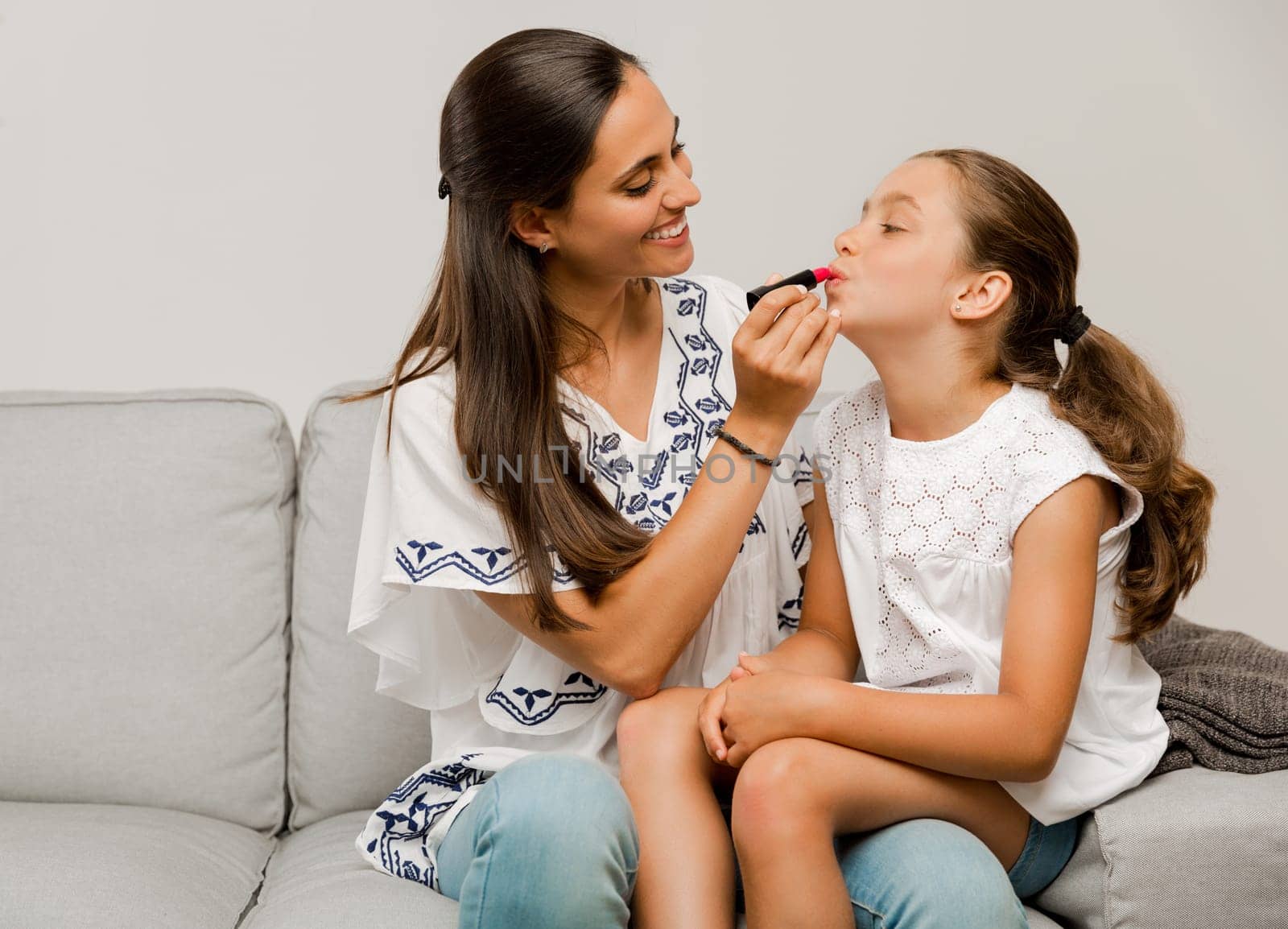 Mother playing with her daughter applying lipstick