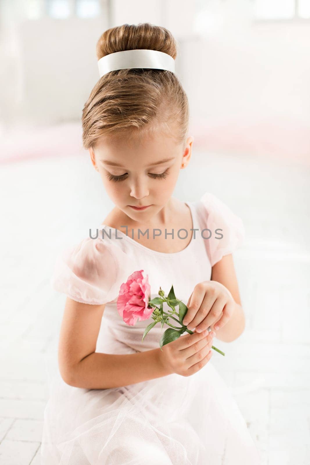 The little balerina in white tutu in class at the ballet school sitanding on the wooden floor with flowers
