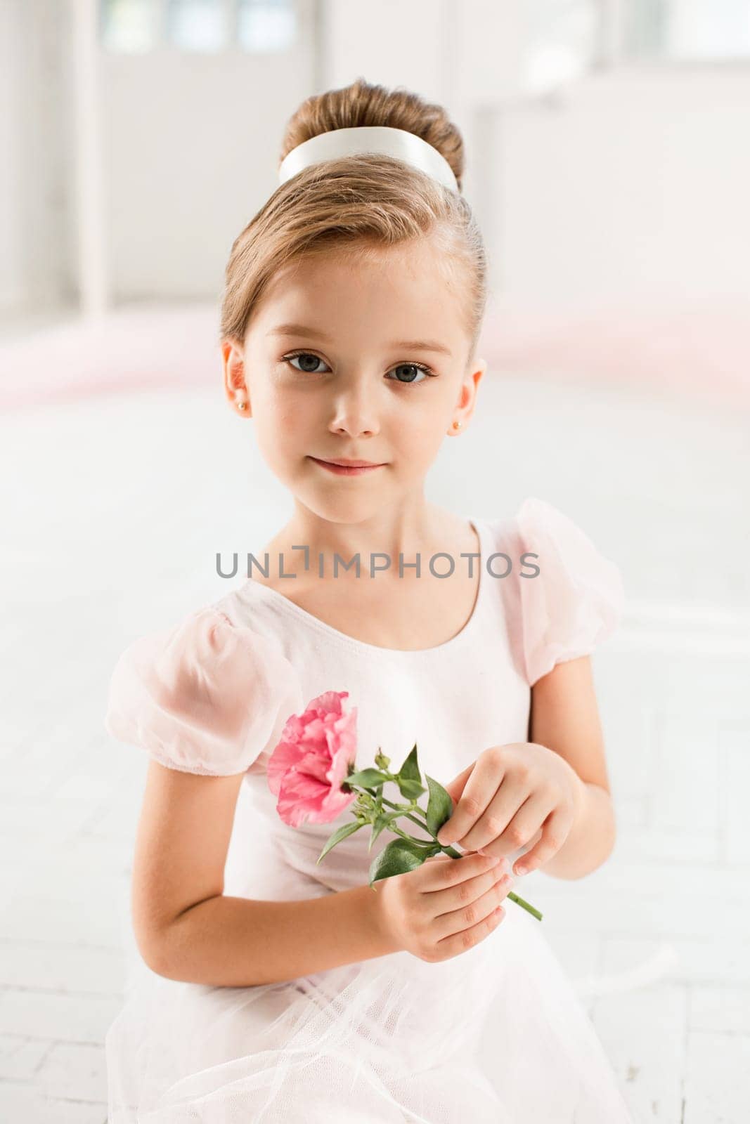 The little balerina in white tutu in class at the ballet school sitanding on the wooden floor with flowers