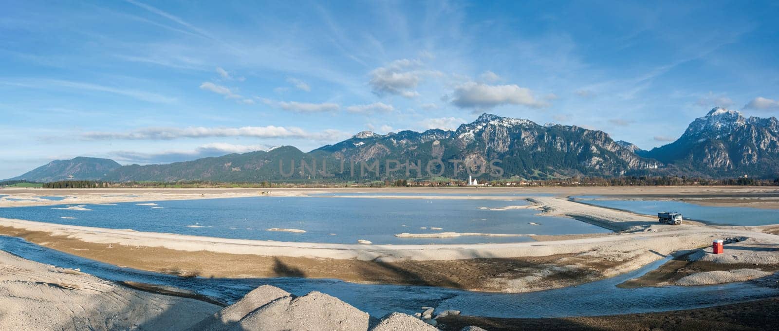 Panoramic view of the drained Forggensee near Füsssen.. The Forggensee,also stored Roßhaupten,is a reservoir crossed by the Lech near Füssen in the Königswinkel in the Bavarian Allgäu. With the meltwater from the surrounding mountains,sedimentary rock and debris settle in the Forggensee,which is collected and transported in winter with drained water,by excavators,bulldozers and other heavy equipment.