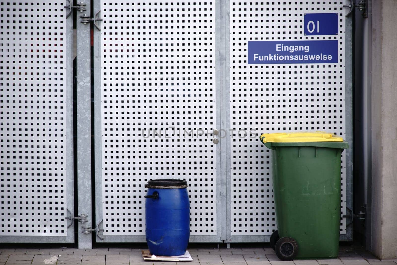 Waste containers stand in front of a lattice gate made of perforated sheet metal.