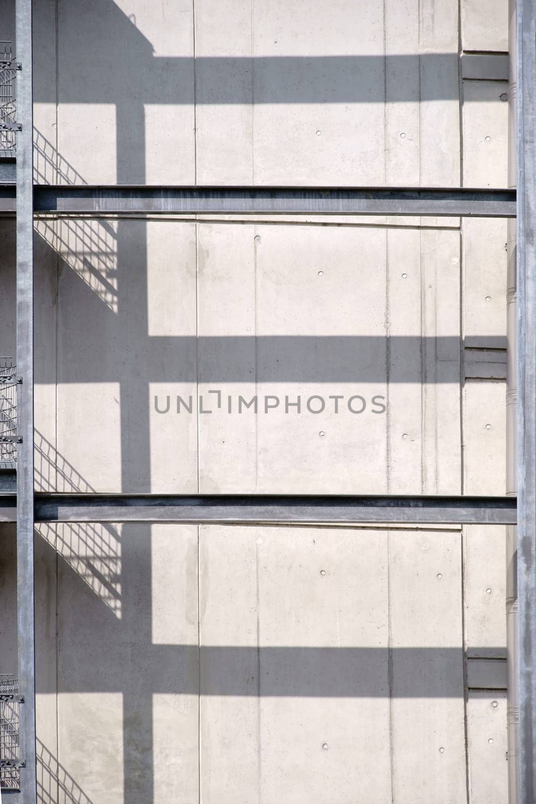 A steel railing with an external staircase casts symmetrical shadows on a concrete wall.