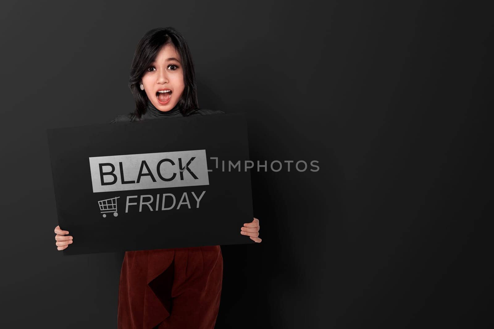 Excited asian woman holding banner with Black Friday announcement over black background