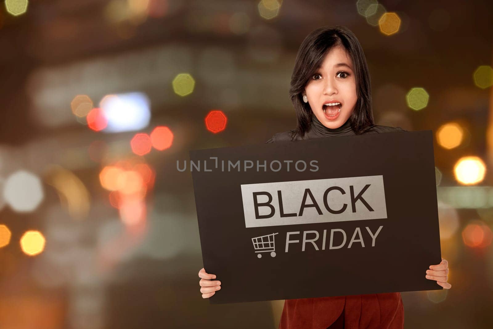 Excited asian woman holding banner with Black Friday announcement against blurred light background
