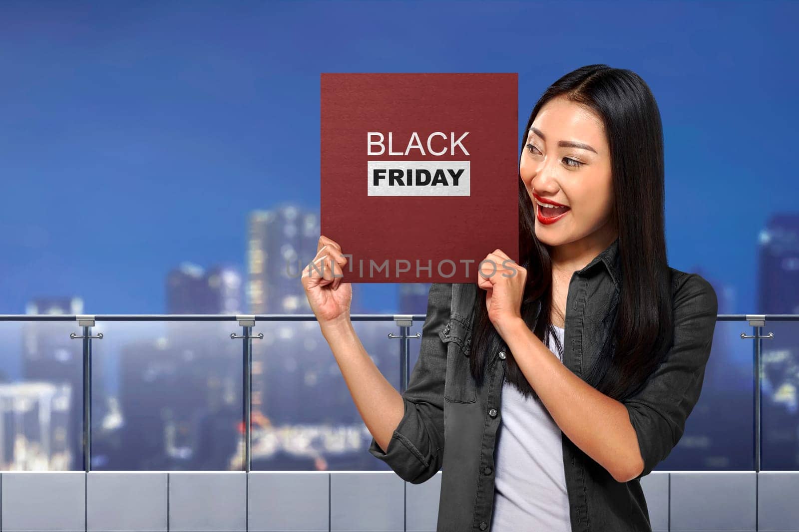 Happy asian woman holding board with Black Friday message over cityscape background