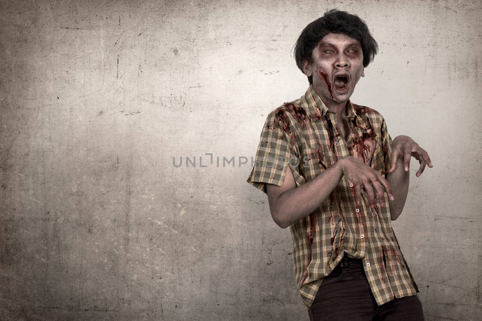 Spooky and bloody asian zombie man in a clothes standing against dirty background