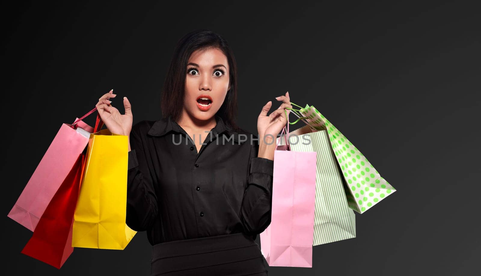 Excited asian woman holding colorful paper bag celebrating Black Friday over black background