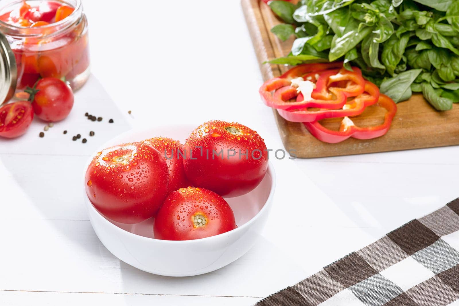 Canned tomatoes and fresh tomatos and other cut vegetables on white background