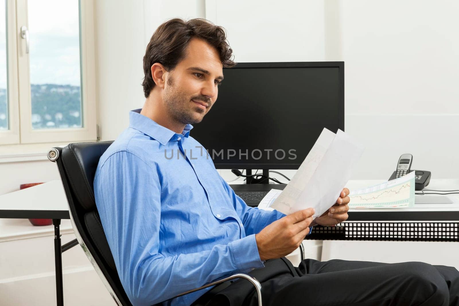 Young businessman sits with documents at a grater table in the office and informs himself