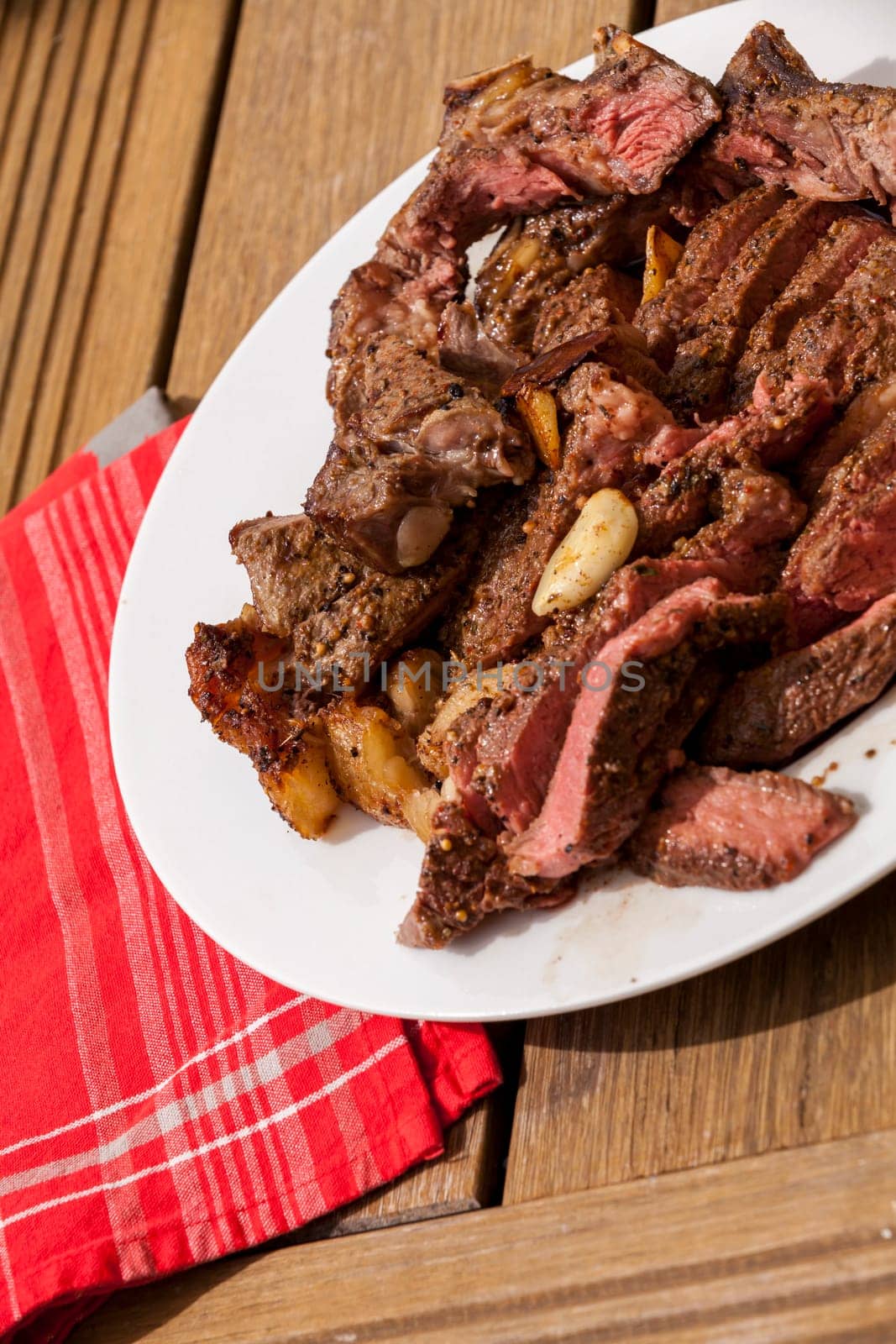 Sliced medium pink cooked beef on a plate with napkin on a wood base