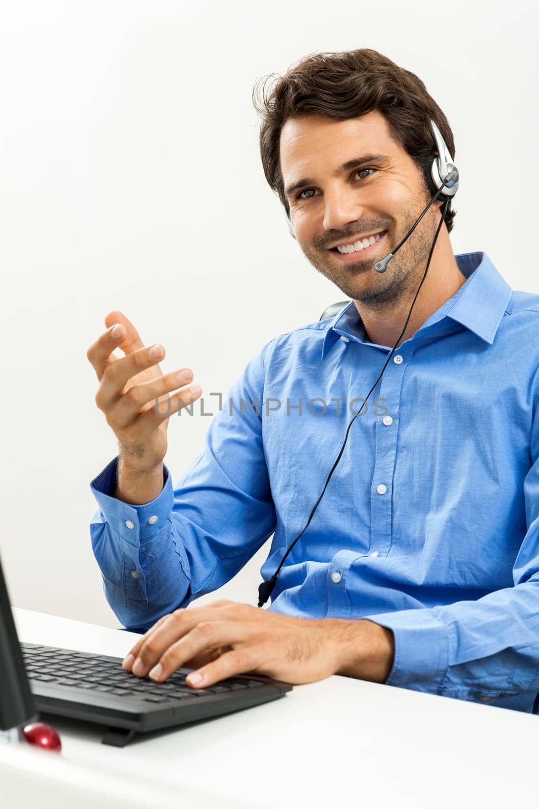 Attractive young man with headset in the office at customer service operator phone service cheerful with blue shirt
