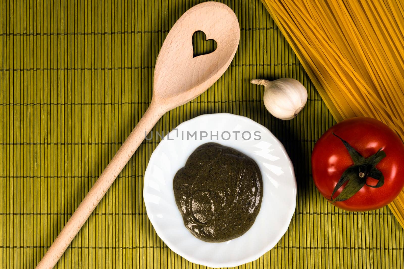 Wooden spoon with Italian food ingredients on green background.