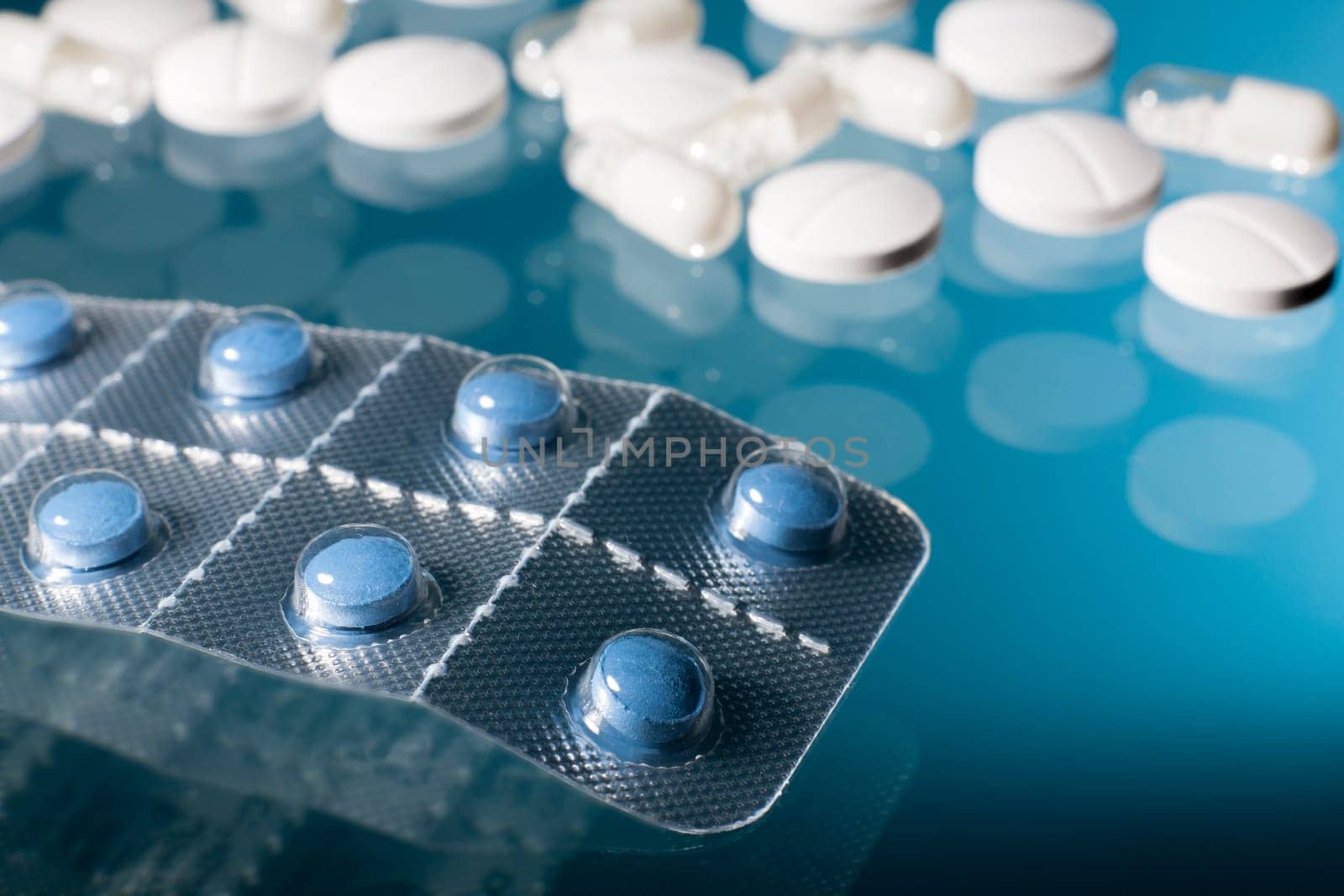 Blue pills in strip with white medicine pills and capsules in blue background