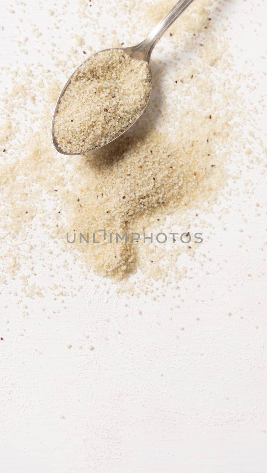 Raw uncooked fonio seeds in a metal spoon on white table top view, copy space. African ancient pseudocereal. Organic super food. Healthy food concept. Gluten free alternative seeds