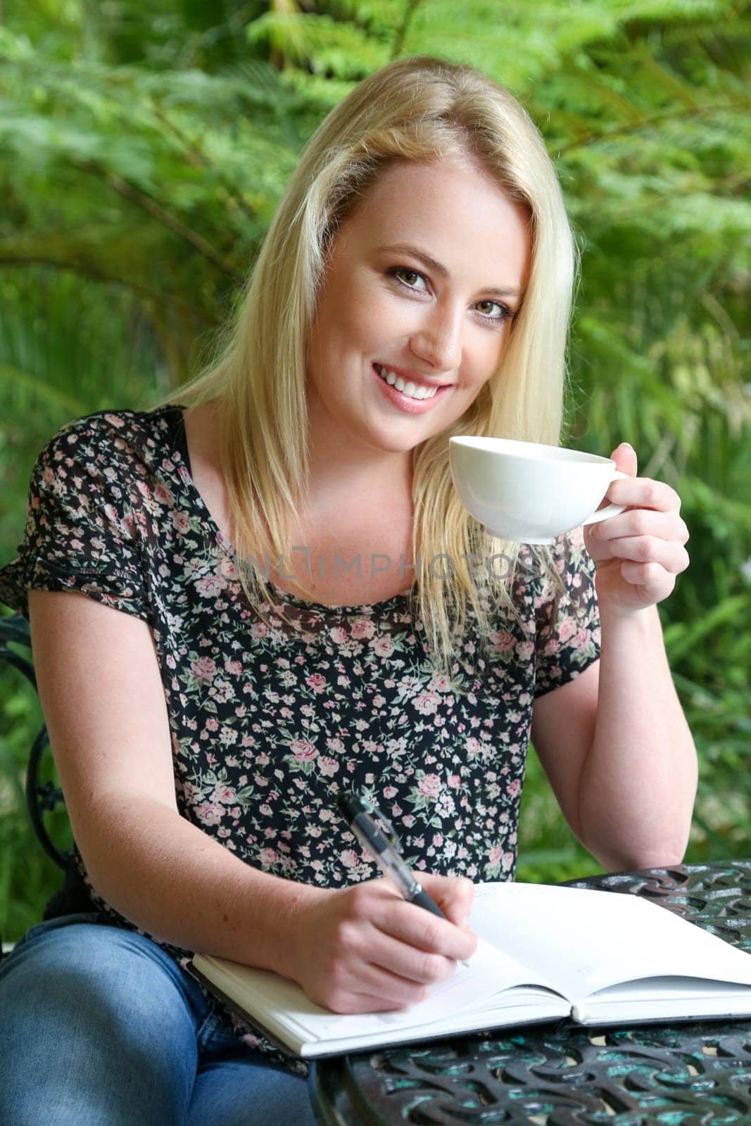 Lovely blond woman writing in her journal while sitting at a table outdoors