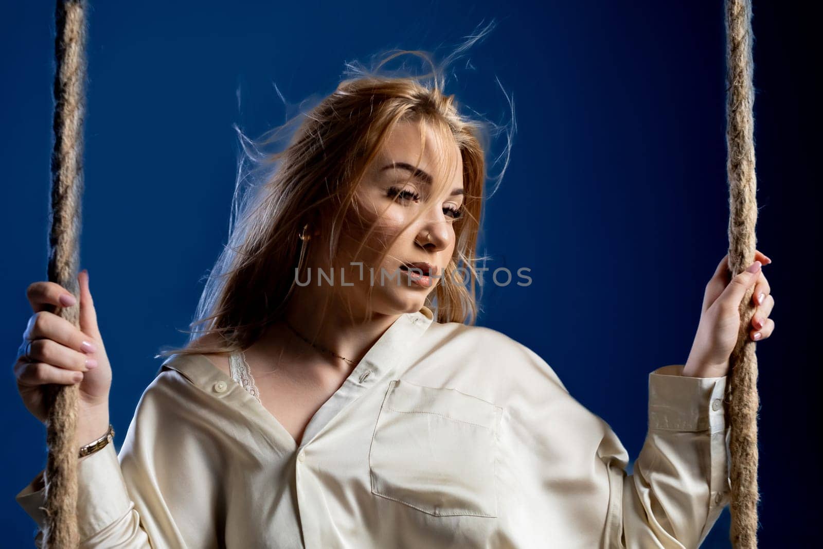 A young woman dressed in a beautiful white outfit gracefully sits upon a swing, exuding a deep contemplative mood